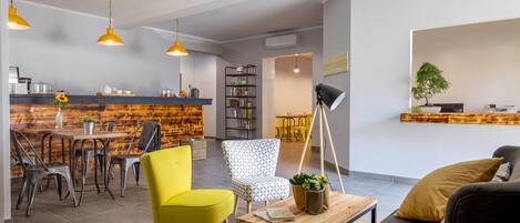 A modern living room with a wooden dining table, yellow and patterned chairs, a sofa, and a floor lamp.
