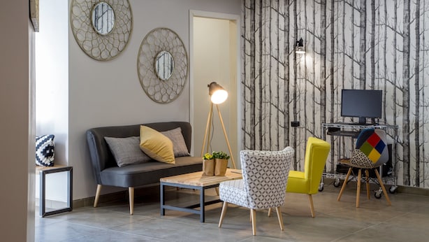 A living room with a sofa, two armchairs, a coffee table, a TV on a stand, and a wall with a tree pattern. - Urban Garden Hotel (Rome)