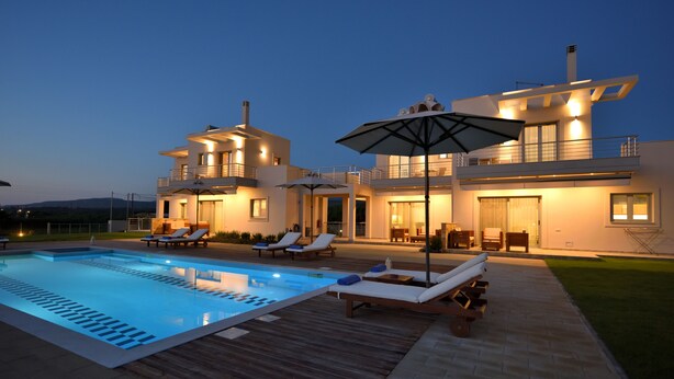 A modern two-story house with a swimming pool, outdoor seating, and a well-lit patio area. - Edem Suites (Trifylia)