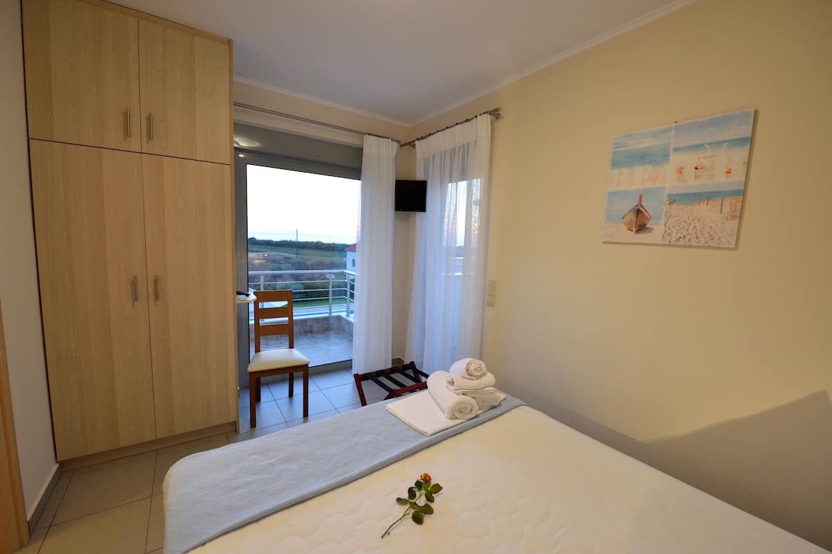 A hotel room with a bed, a chair, a desk, a wardrobe, and a painting on the wall.