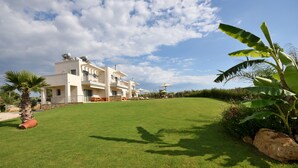 A modern multi-story building with a well-maintained lawn and a few palm trees. - Edem Suites (Trifylia)