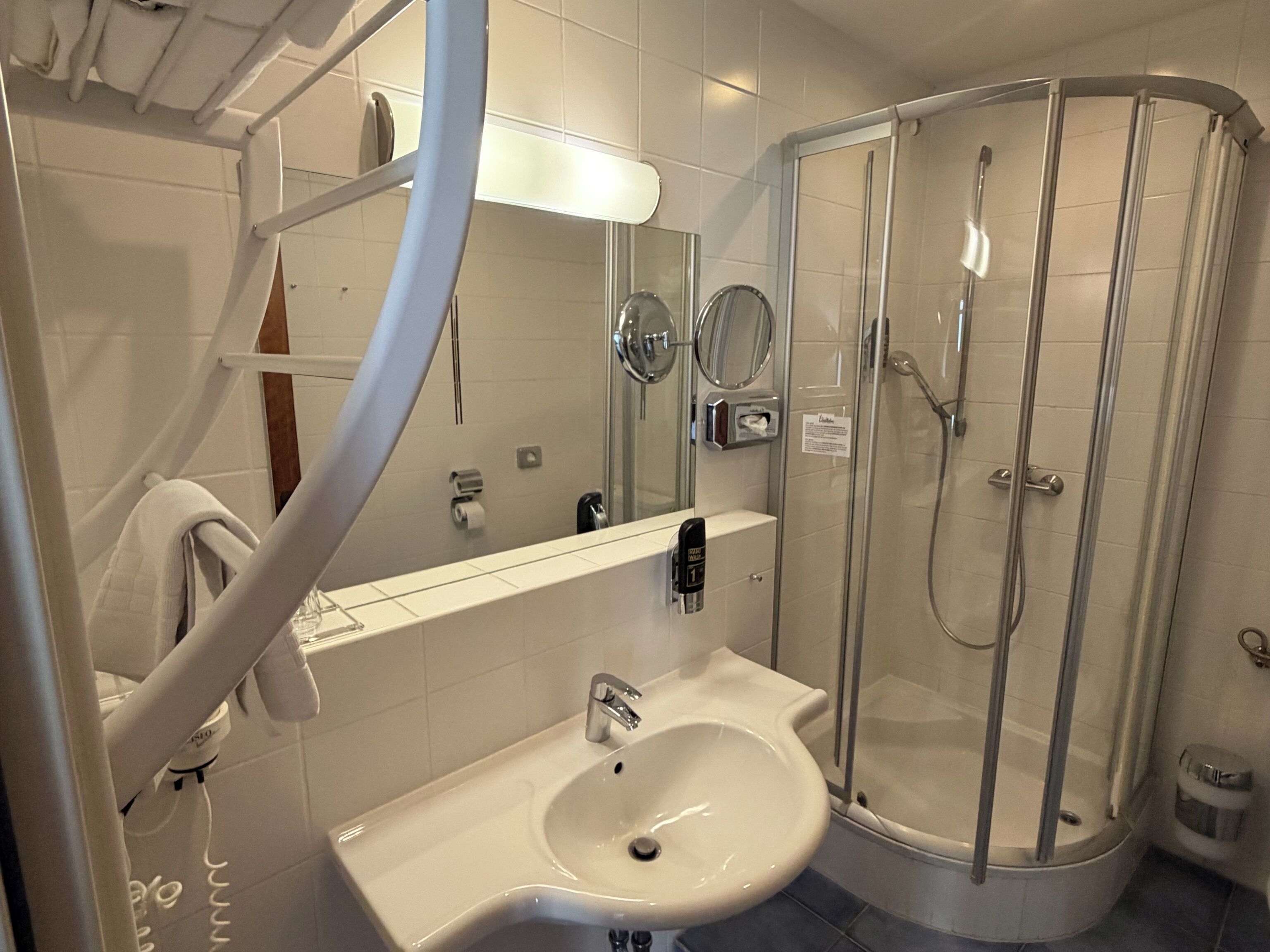 Une salle de bain équipée d’un lavabo, d’un miroir, d’un porte-serviettes et d’une douche à parois de verre.