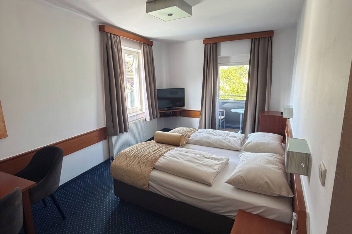 Habitación de hotel con cama, escritorio, silla, televisor y vistas al exterior.