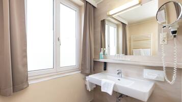 Un baño moderno con un ventanal grande, un lavamanos, un espejo y un secador de pelo.