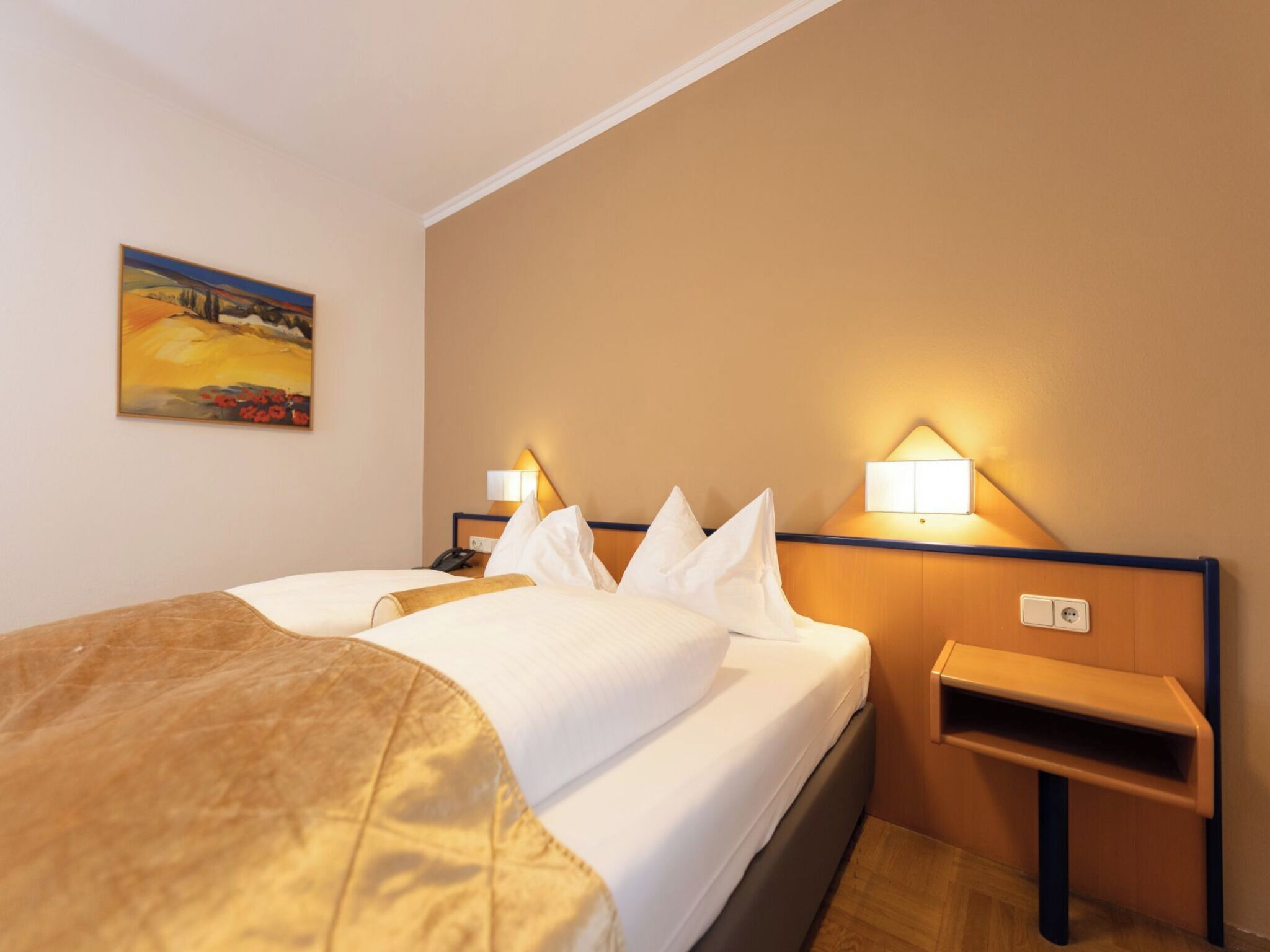 A hotel room with a bed, bedside tables, lamps, and a painting on the wall.