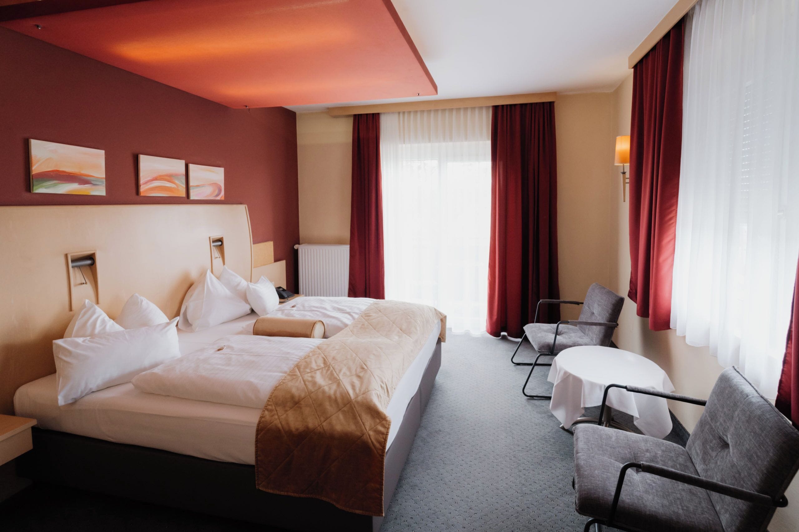 Ein Hotelzimmer mit einem großen Bett, zwei Sesseln, einem kleinen Tisch und Kunstwerken an der Wand.