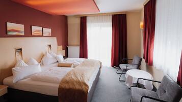 Ein Hotelzimmer mit einem großen Bett, zwei Sesseln, einem kleinen Tisch und Kunstwerken an der Wand.