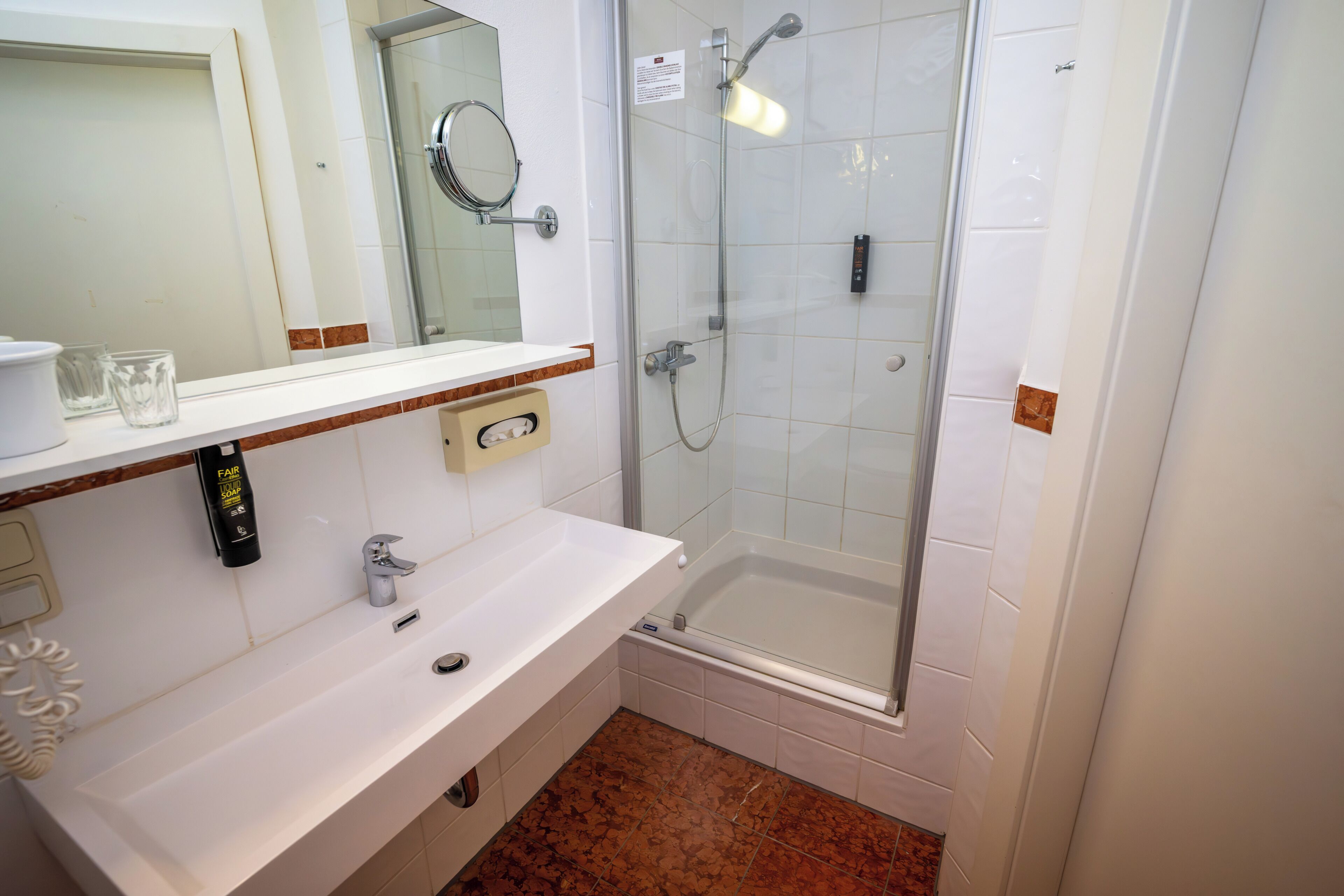 A bathroom with a white sink, a mirror, a shower, and a toilet.