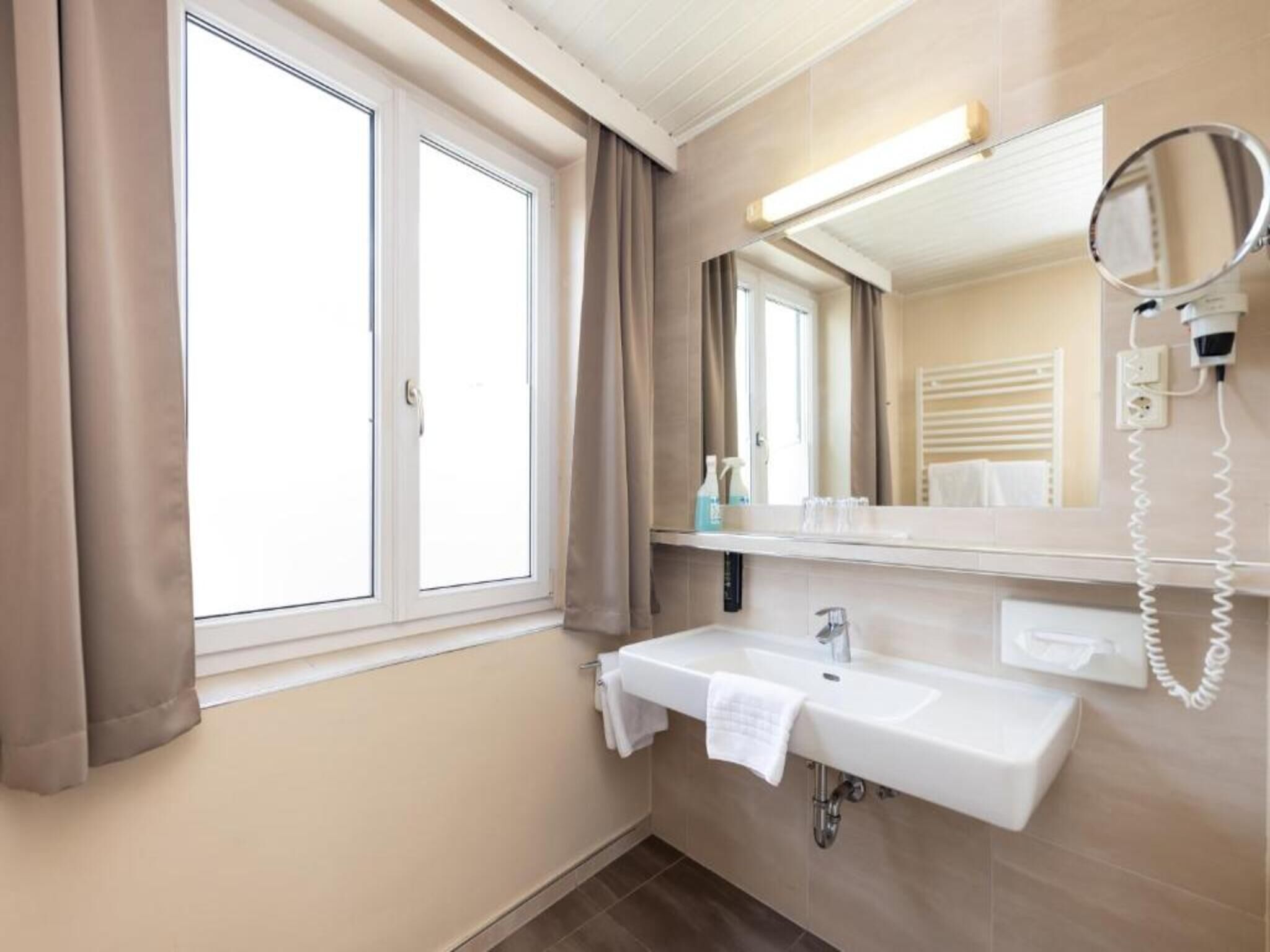A bathroom with a window, a sink, a mirror, and a hairdryer.