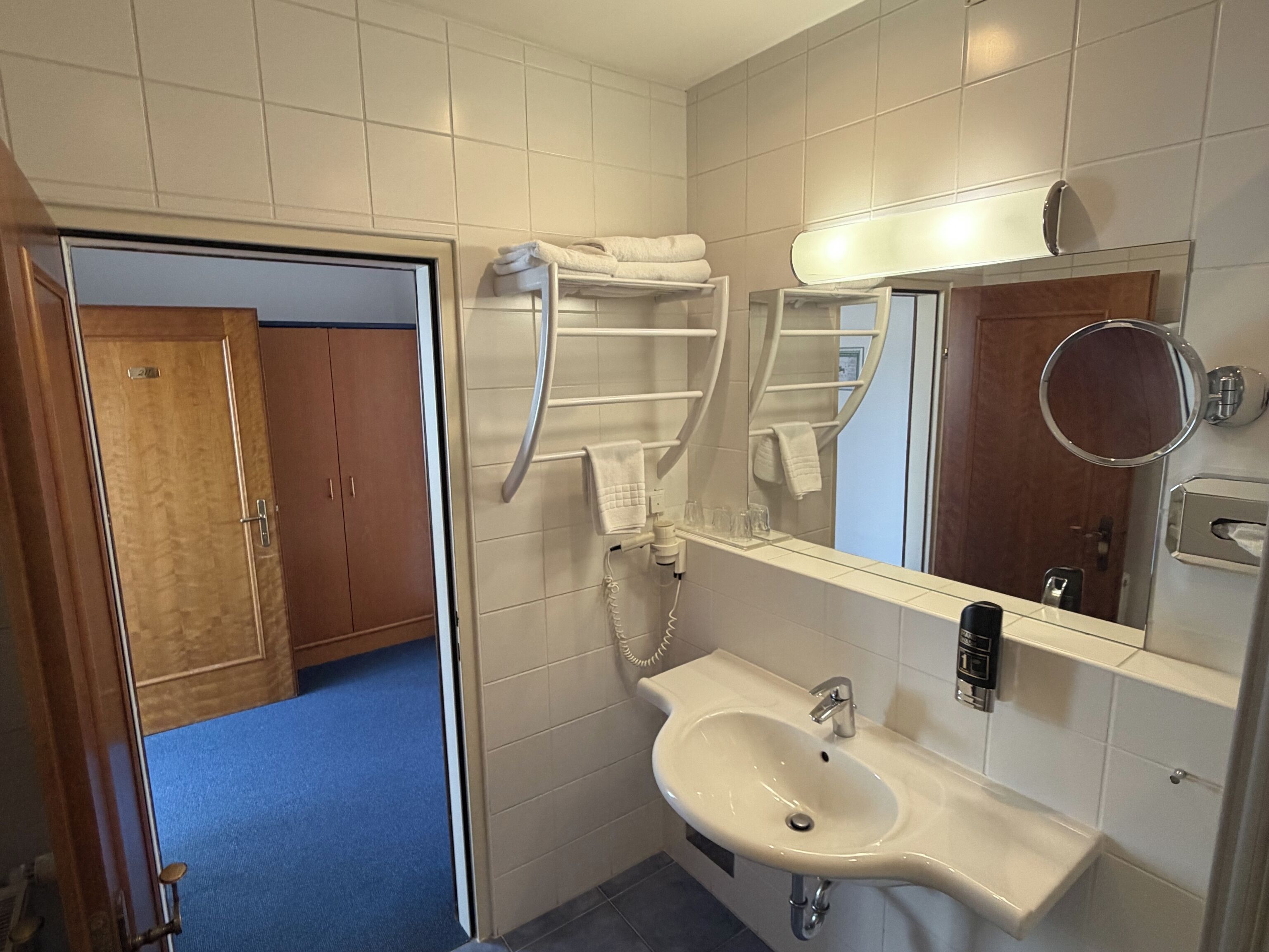 A hotel bathroom with a sink, mirror, towel rack, and a shower area.