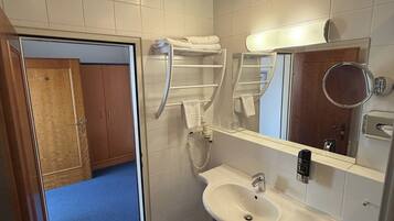 A hotel bathroom with a sink, mirror, towel rack, and a shower area.