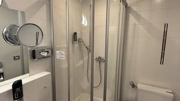 Cabina de ducha con paredes de vidrio, zona de lavado de manos, inodoro y espejo.