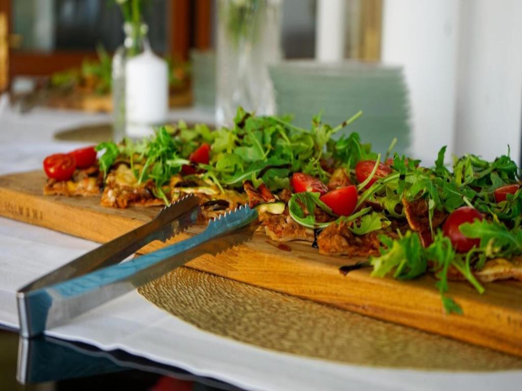 Une planche à découper en bois sur laquelle se trouve une salade, un couteau et une nappe blanche.