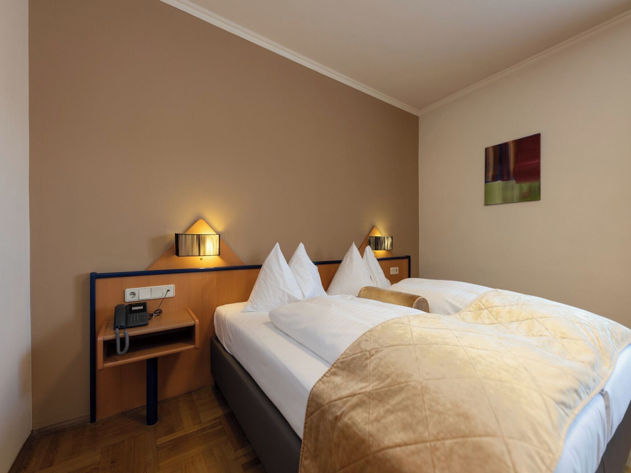 Une chambre d’hôtel avec un lit, des lampes de chevet, un téléphone et un tableau au mur.