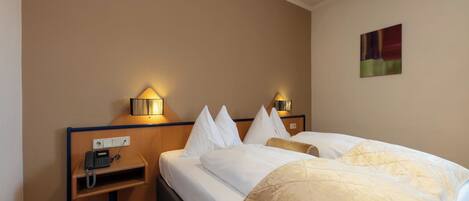 A hotel room with a bed, bedside lamps, a telephone, and a painting on the wall.