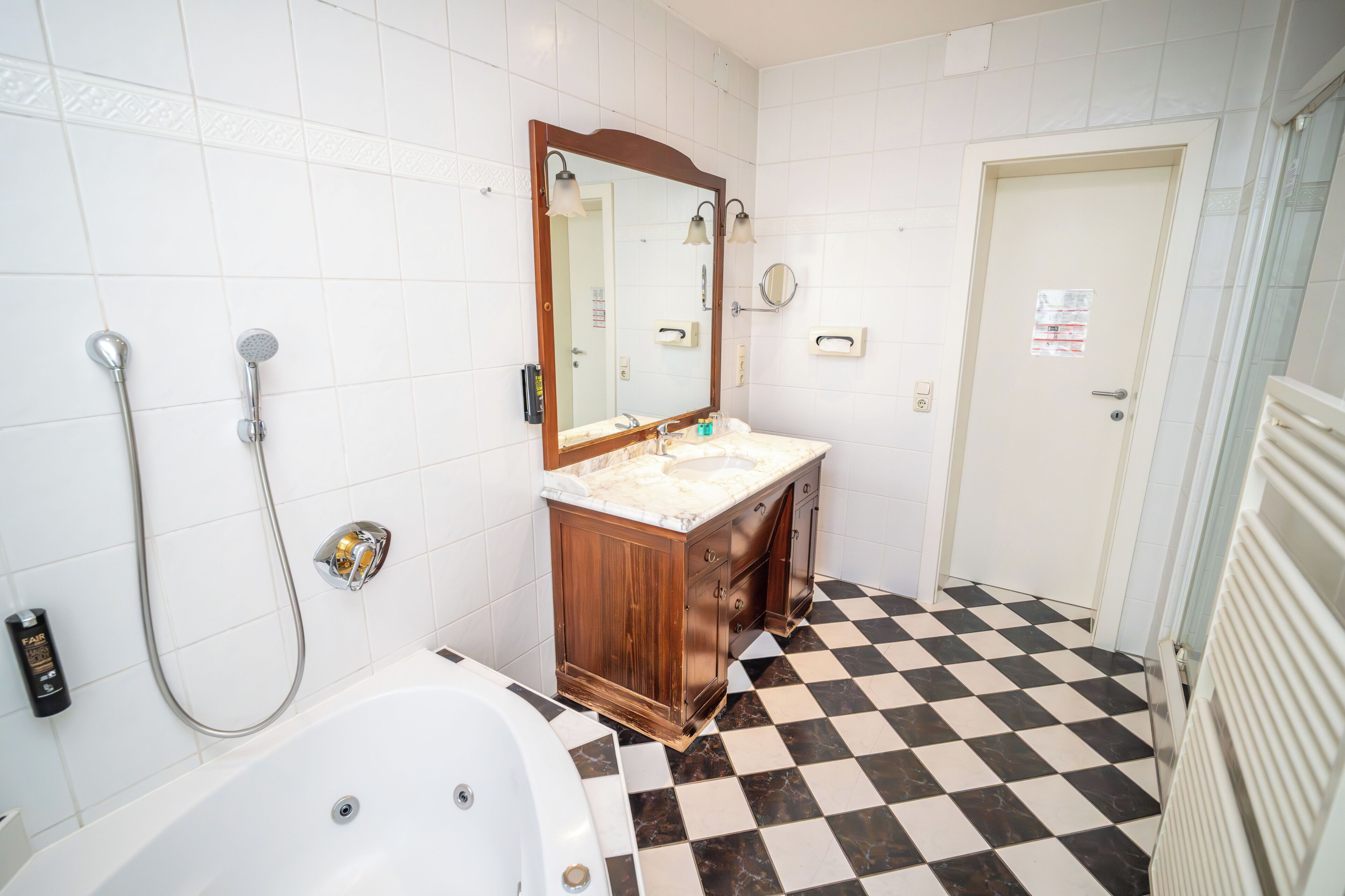 A bathroom with a checkered floor, a white bathtub, a wooden vanity with a mirror, and a shower with a handheld showerhead.
