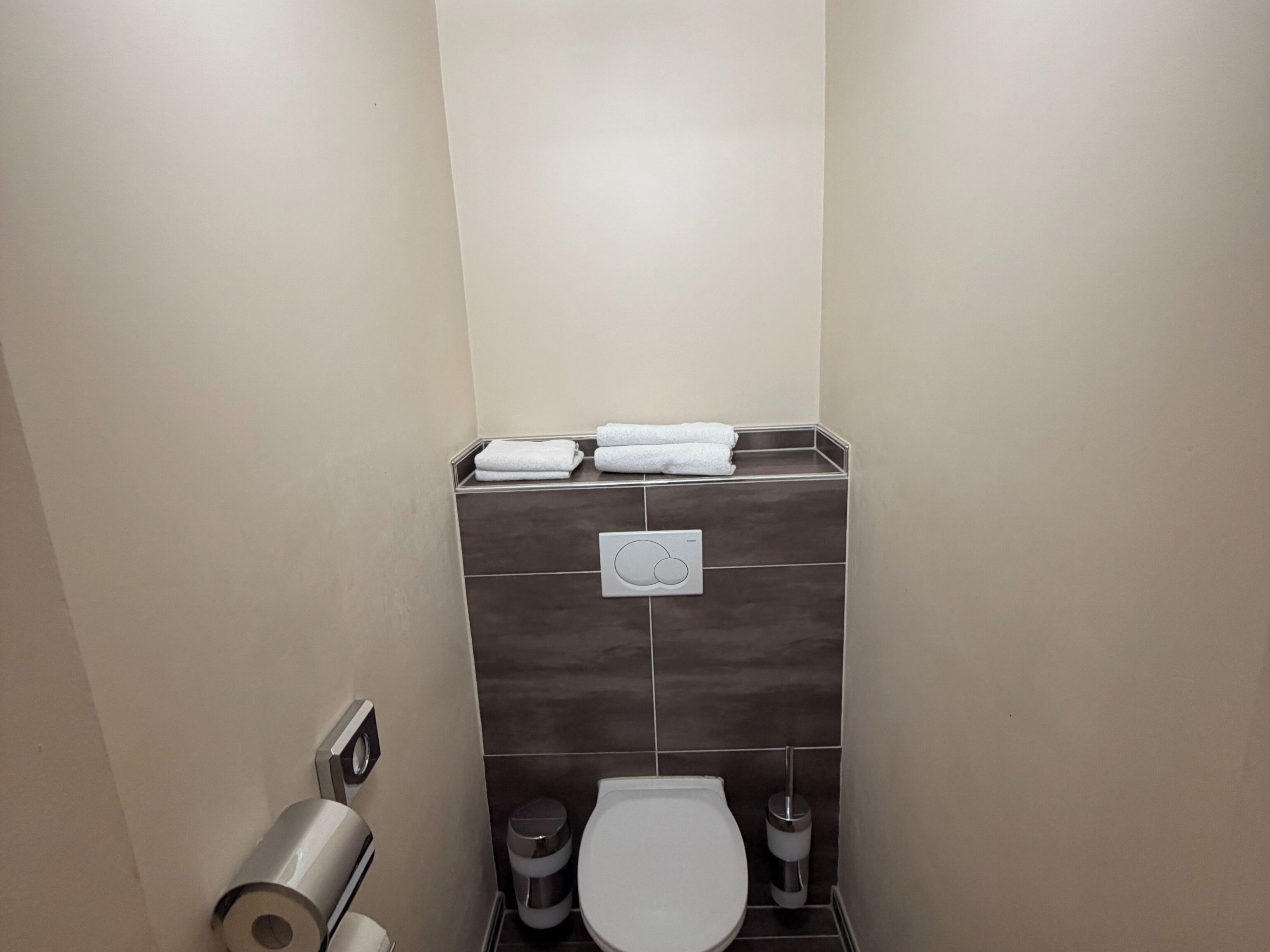 Une petite salle de bain comprenant des toilettes, une poubelle, un distributeur de serviettes et un porte-rouleau de papier toilette.