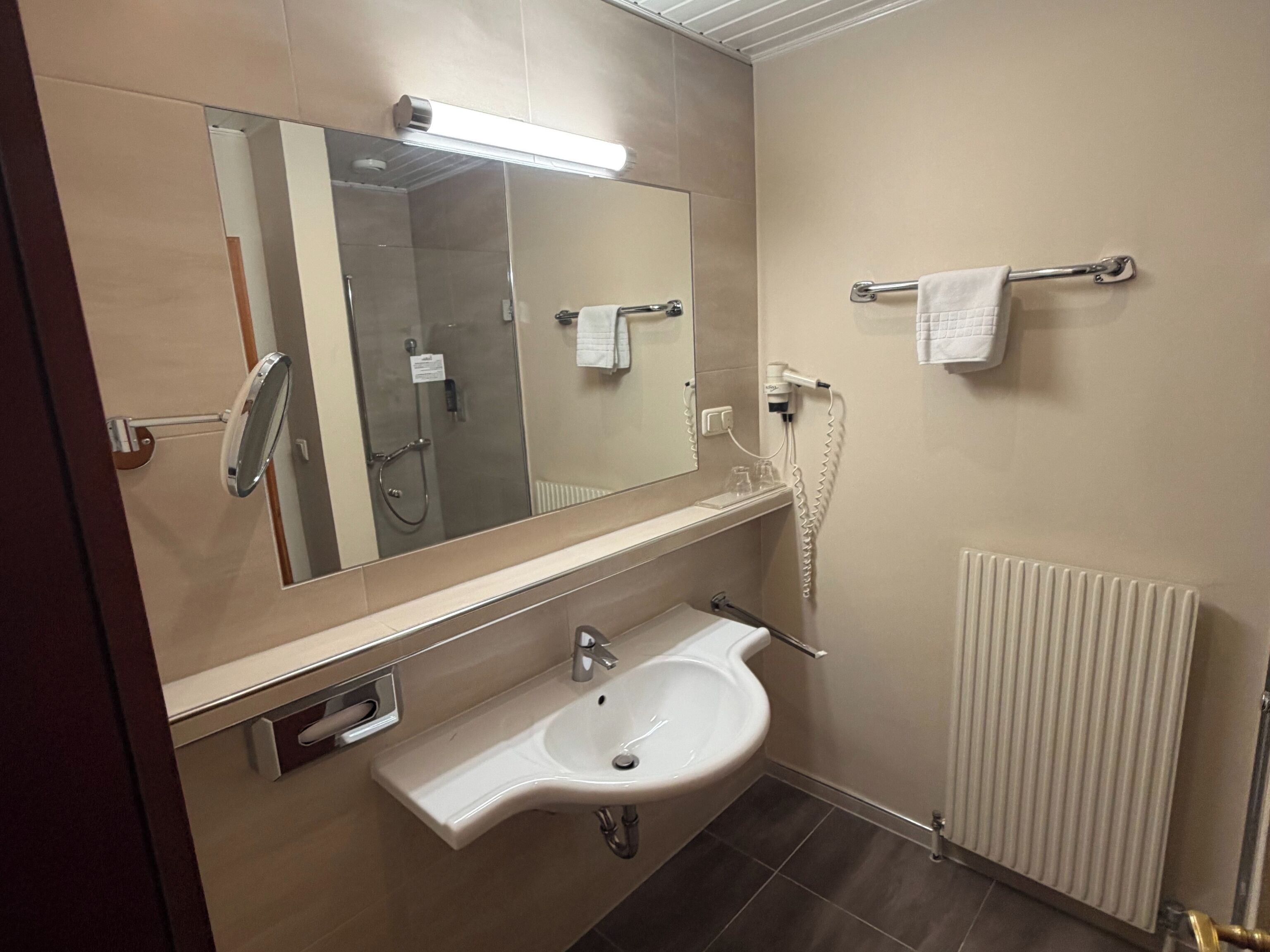 Un baño con lavabo, espejo, toallero y ducha.