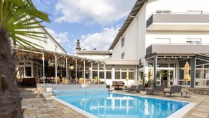 Ein Pool mit Liegestühlen, eine überdachte Terrasse und ein Gebäude mit großen Fenstern.