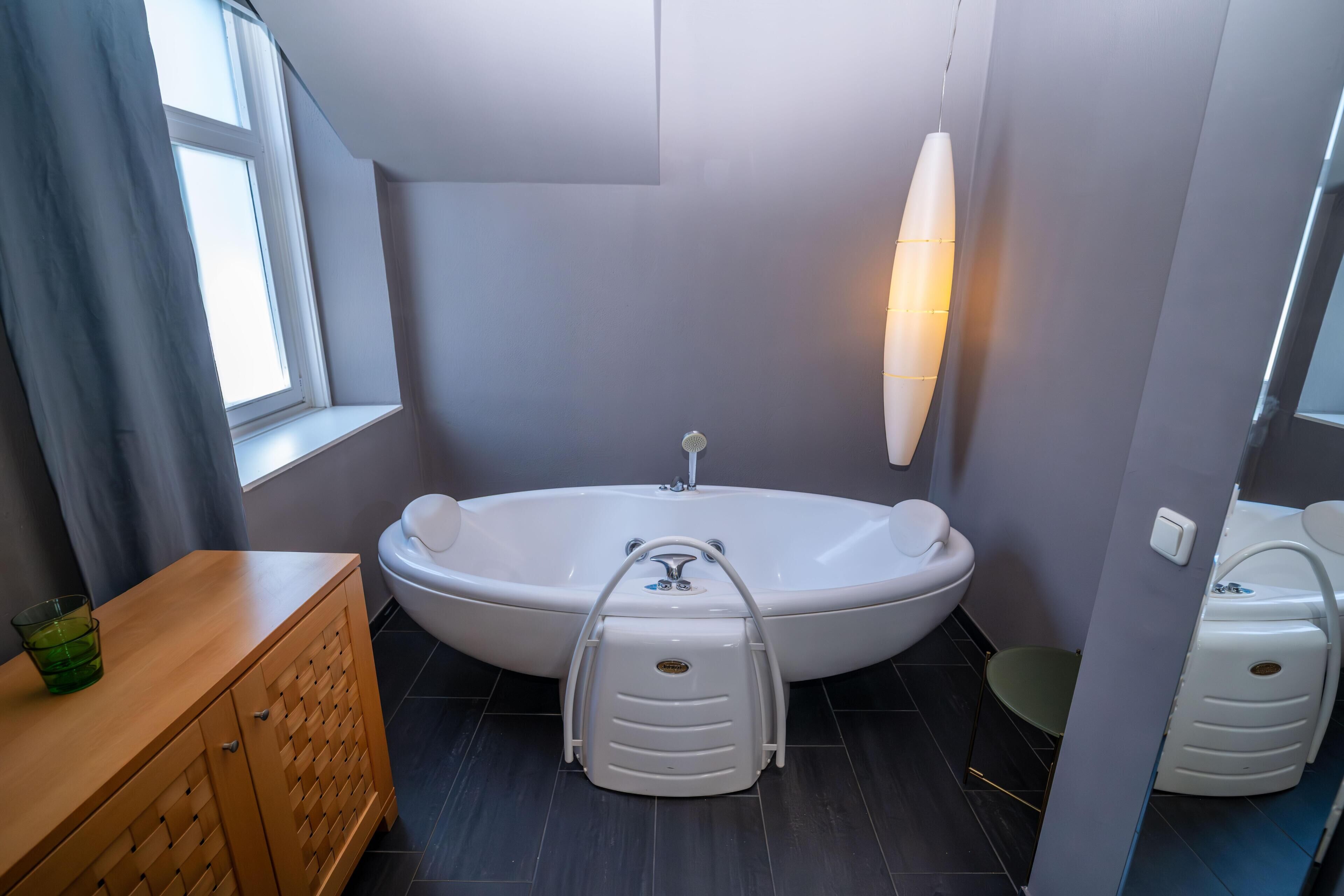 A modern bathroom with a freestanding bathtub, a wooden vanity, and a window with curtains.