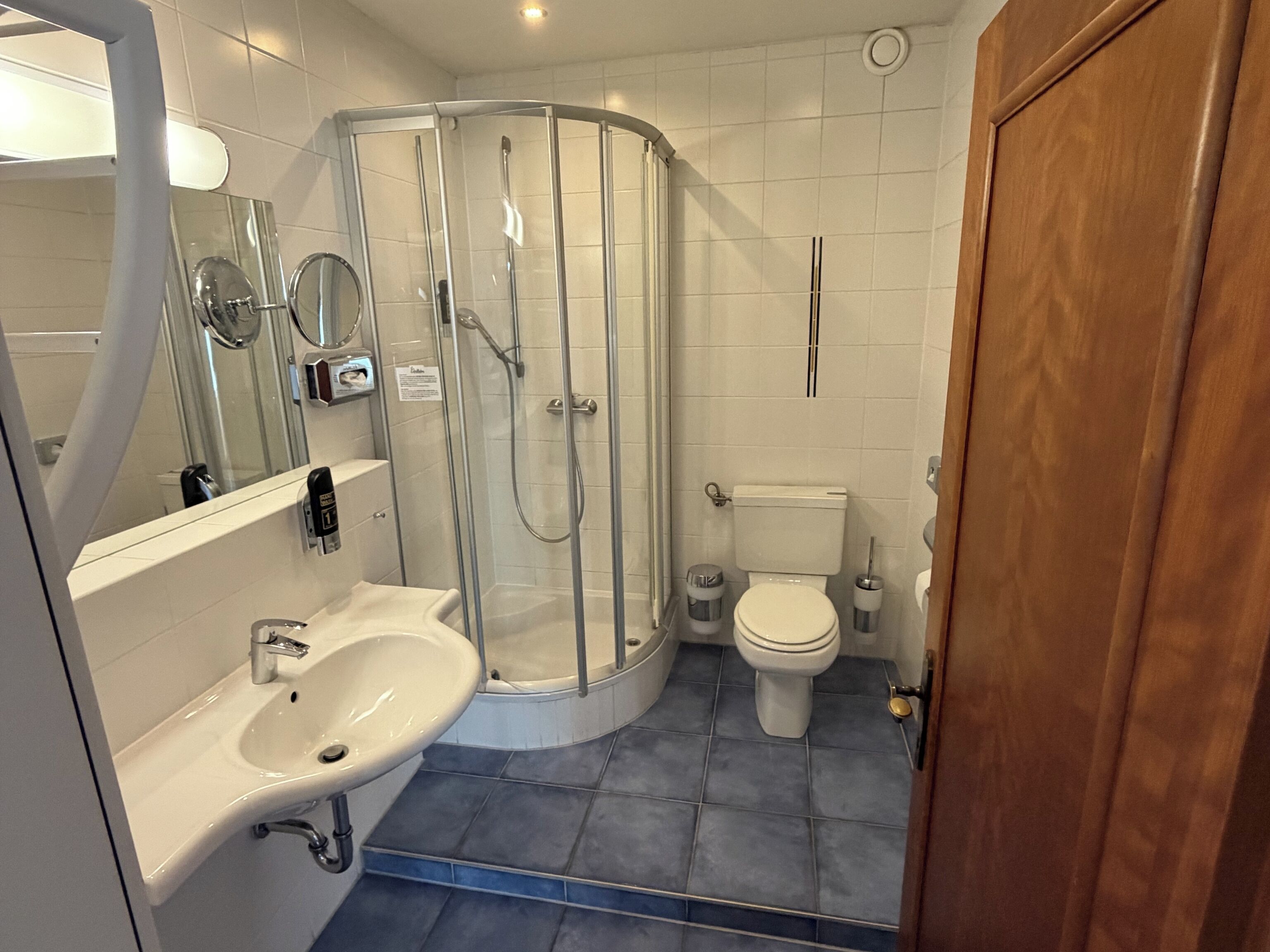 Une salle de bain moderne avec une douche à parois de verre, des toilettes blanches et un lavabo avec un miroir.