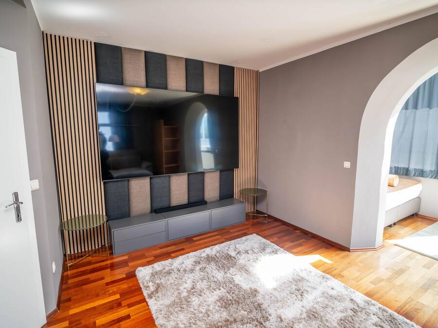 A modern living room with a large flat-screen TV, wooden flooring, a fluffy rug, and a built-in bench with storage.