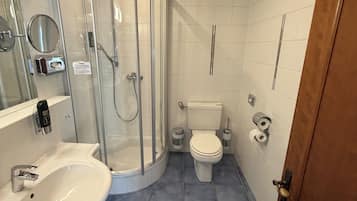 A bathroom with a glass-enclosed shower, a white sink, a toilet, and a door with a brass handle.