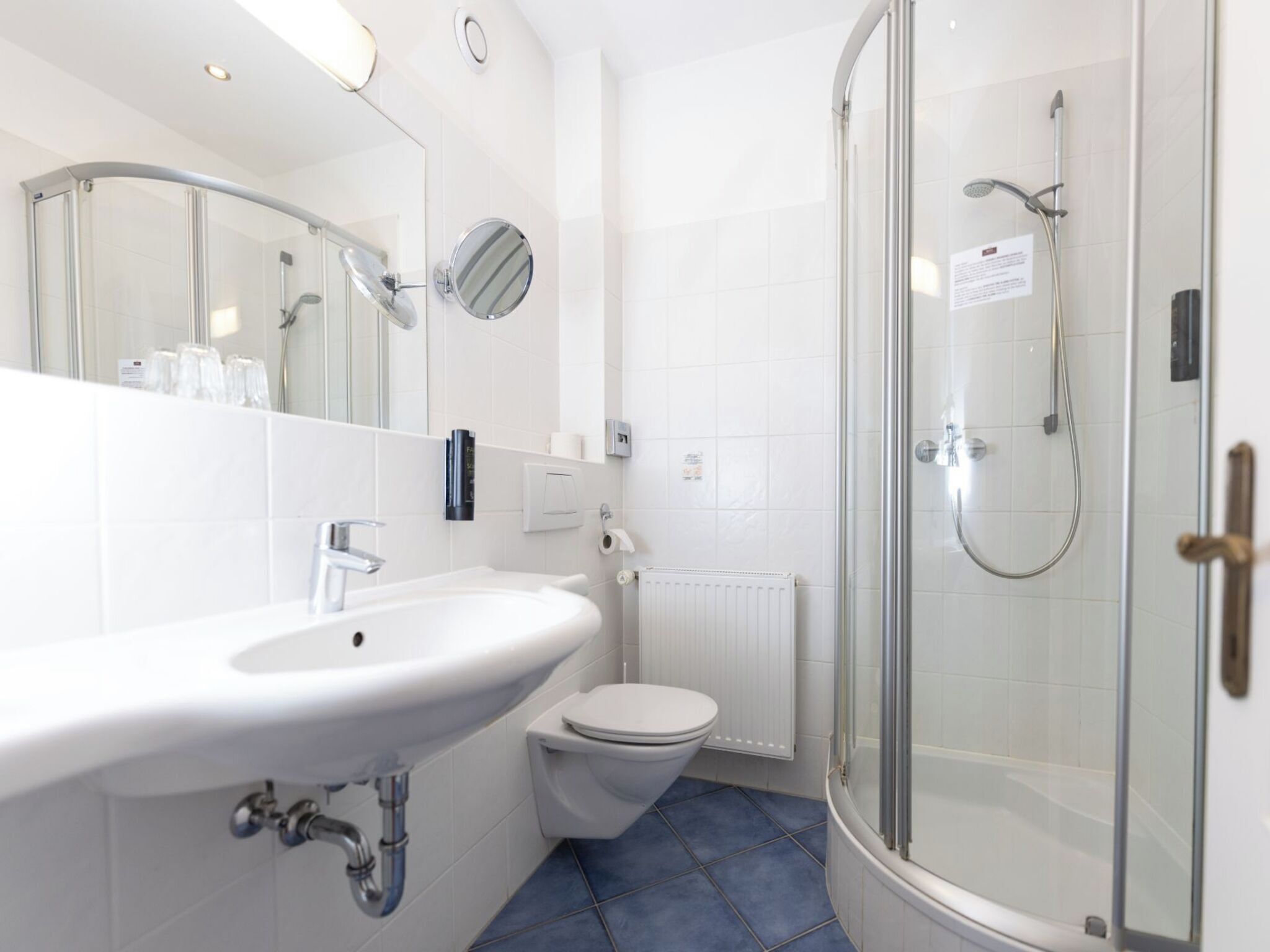 Un baño moderno con lavamanos blanco, inodoro y ducha con mampara de vidrio.