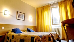 A hotel room with a bed, two bedside lamps, a framed picture on the wall, and a window with yellow curtains. - Hôtel Fouillade (Argentat-sur-Dordogne)