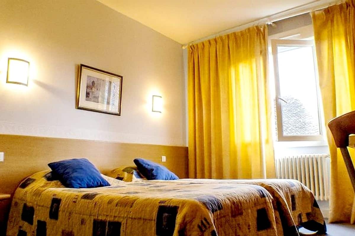 A hotel room with a bed, two bedside lamps, a framed picture on the wall, and a window with yellow curtains.