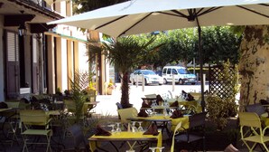 An outdoor dining area with yellow tables and chairs, umbrellas, and a street view in the background. - Hôtel Fouillade (Argentat-sur-Dordogne)