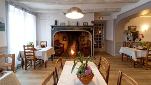 A dining area with a fireplace, wooden furniture, and a table with a potted plant. - Hôtel Fouillade (Argentat-sur-Dordogne)