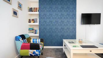 Una habitació amb un butac armchair de colors, una estanteria, un escriptori amb un ordinador i una cortina blava amb un dibuix gran.