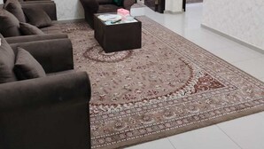 A spacious living room with a large brown sofa set, a coffee table, and a patterned rug. There is a door leading to another room.
