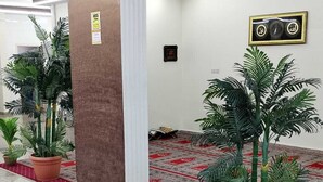 A hallway with tiled flooring, potted plants, a patterned carpet, and a wall-mounted security camera.
