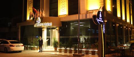 A hotel entrance with a sign reading "Grand Marriot Hotel," potted plants, and a white car parked in front.