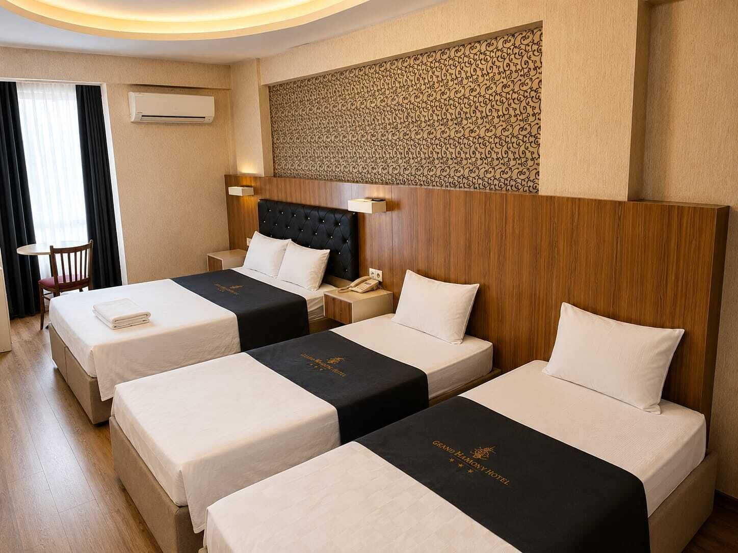 Habitación de hotel con tres camas, cabecera de madera, aire acondicionado instalado en la pared y una mesita con una silla.
