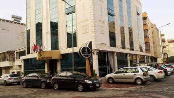 Un hotel con fachada moderna, varios pisos y un estacionamiento con varios coches.