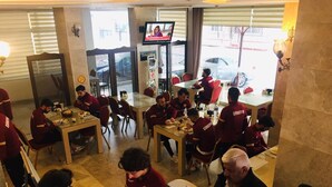 Un comedor con varias mesas y sillas, un televisor en la pared y vista a la calle.