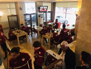 Un espace repas comprenant plusieurs tables et chaises, un téléviseur fixé au mur et donnant sur la rue.