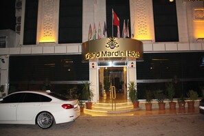 The Grand Mardini Hotel entrance with flags, a car parked in front, and potted plants around. - Grand Mardini Hotel (Mersin)