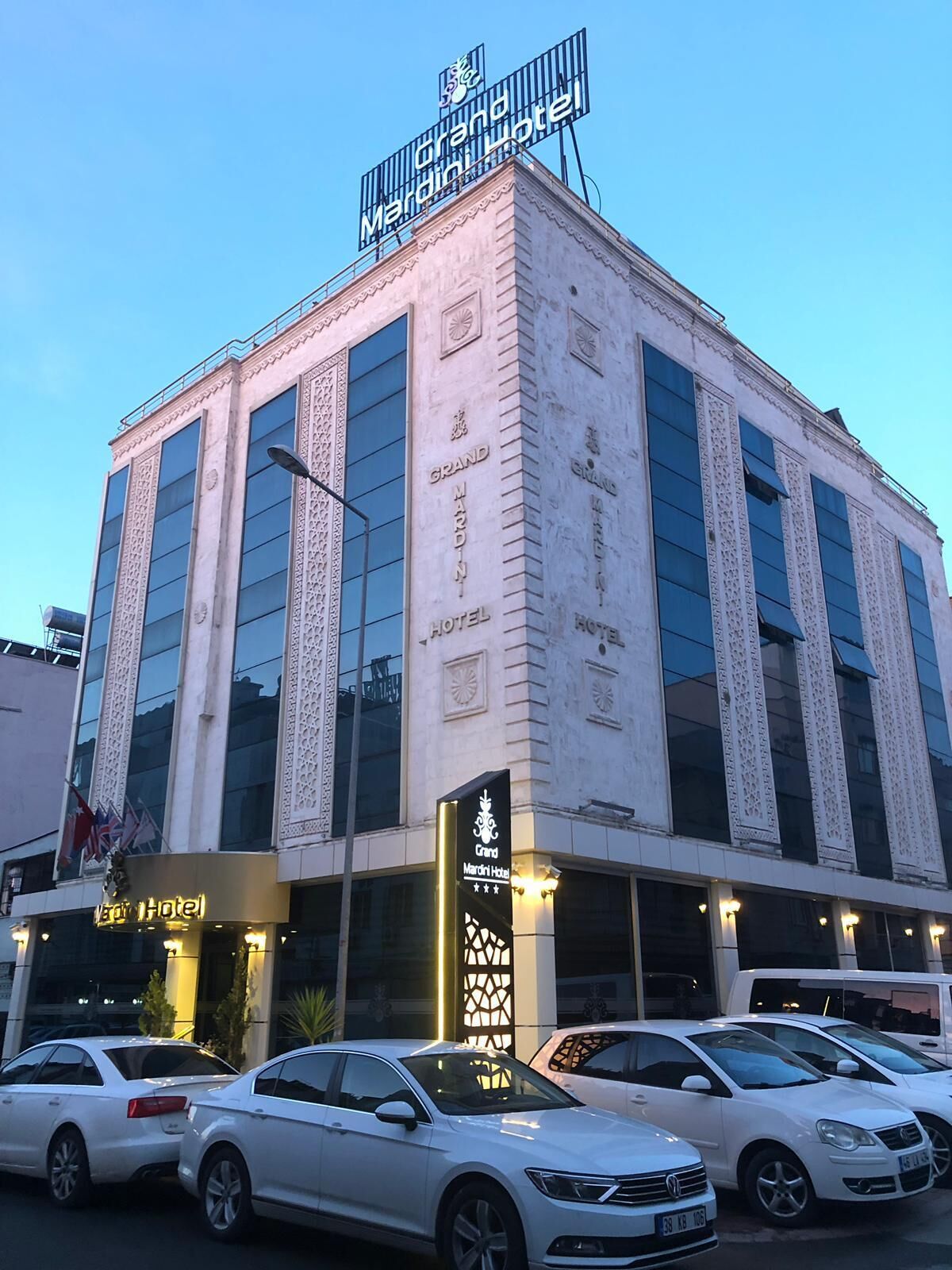 A hotel with a prominent sign reading "Grand Mardin Hotel" and a modern architectural design with large windows and decorative elements.