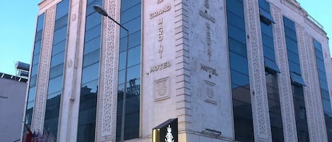 Un hotel con un letrero llamativo que dice "Grand Mardin Hotel" y un diseño arquitectónico moderno con ventanas grandes y elementos decorativos.