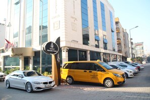 Grand Mariani Hotel met een modern gevel, een gele bestelwagen ervoor geparkeerd en meerdere auto's langs de straat.