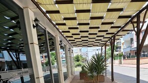 Un espacio al aire libre techado con un camino pavimentado, una palmera y un edificio con grandes ventanales.
