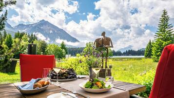 A dining table set outdoors with a mountain view, a statue, and a lake in the background.