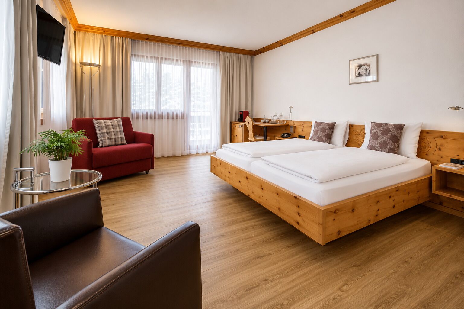 Ein Hotelzimmer mit einem hölzernen Bett, einem roten Sofa, einem kleinen Tisch mit einer Pflanze und einem Schreibtisch mit einer Lampe.