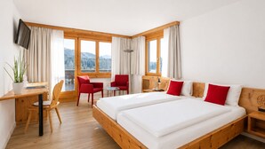 A hotel room with a large bed, a desk with a chair, a small table with two chairs, and a TV mounted on the wall.