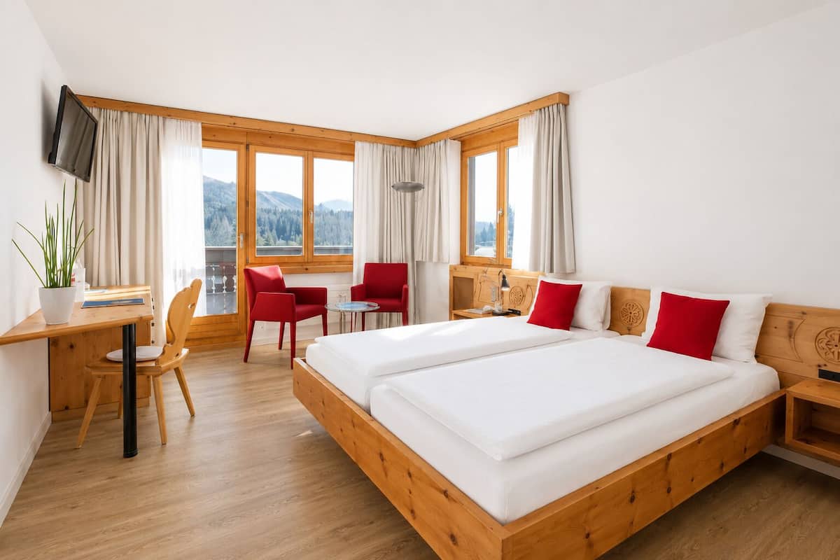 Une chambre d’hôtel avec un grand lit, un bureau avec une chaise, une petite table avec deux chaises et un téléviseur fixé au mur.