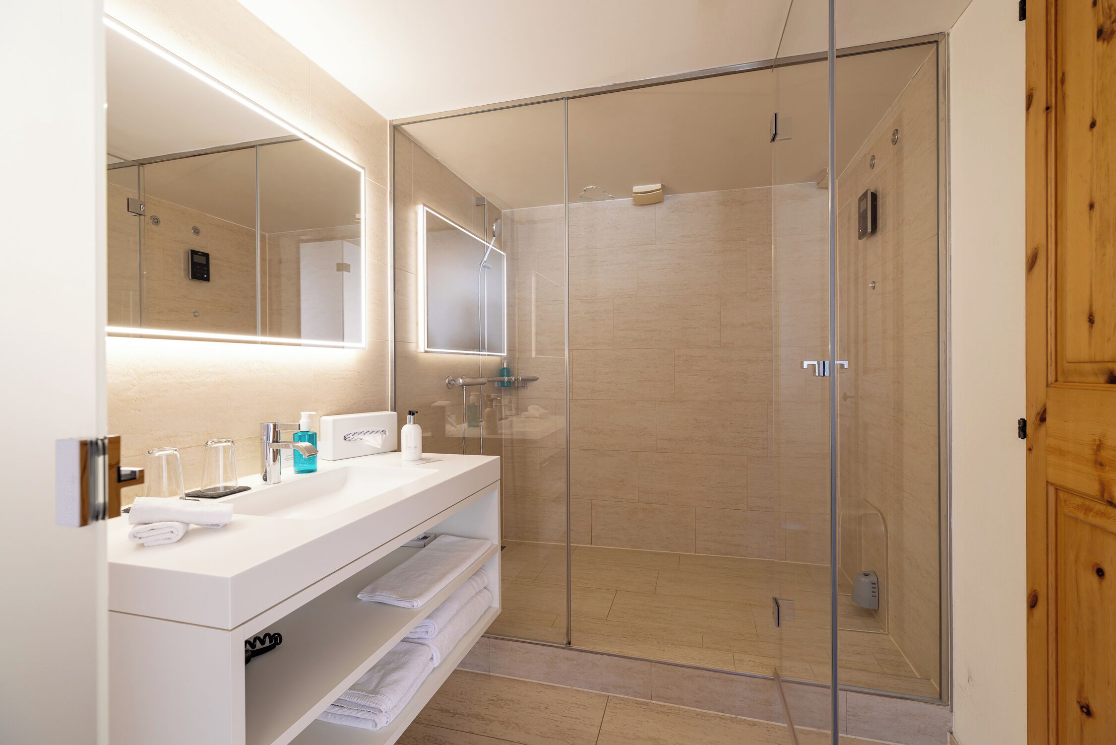 Une salle de bain moderne avec une douche à parois de verre, un meuble-lavabo blanc avec un miroir et une porte en bois.